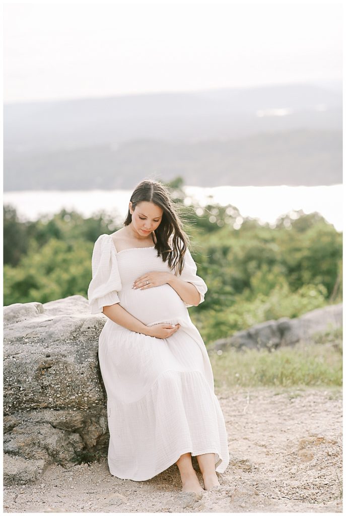 expecting mother leans on rock and looks at belly