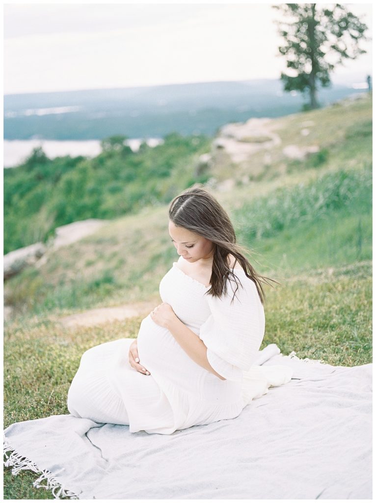 Expecting mother sitting in grass and gazing down at belly, Weathington Park maternity session