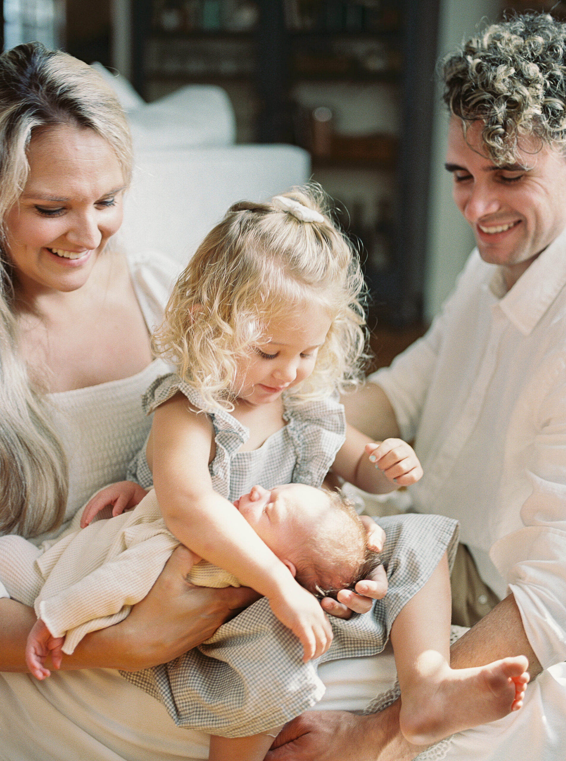 a mother, father, toddler girl and newborn baby cuddle up at a cozy lifestyle newborn session